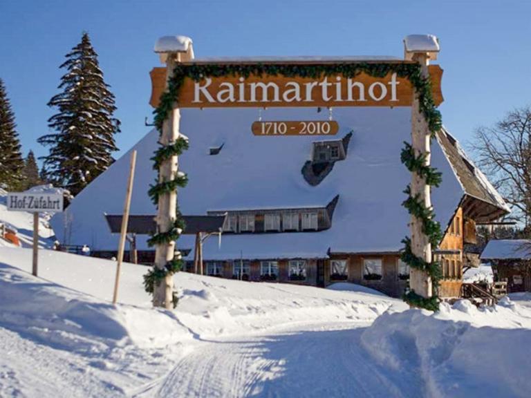 Verschneiter Raimartihof im Schwarzwald mit geschmücktem Torbogen, traditioneller Bauernhof und Ziel der Fondue-Schneeschuhwanderung